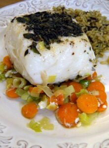 A piece of cooked Halibut over leeks and carrots.