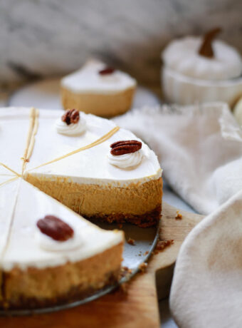 A pumpkin pie cheesecake with sour cream topping and pecan garnish cut into slices.