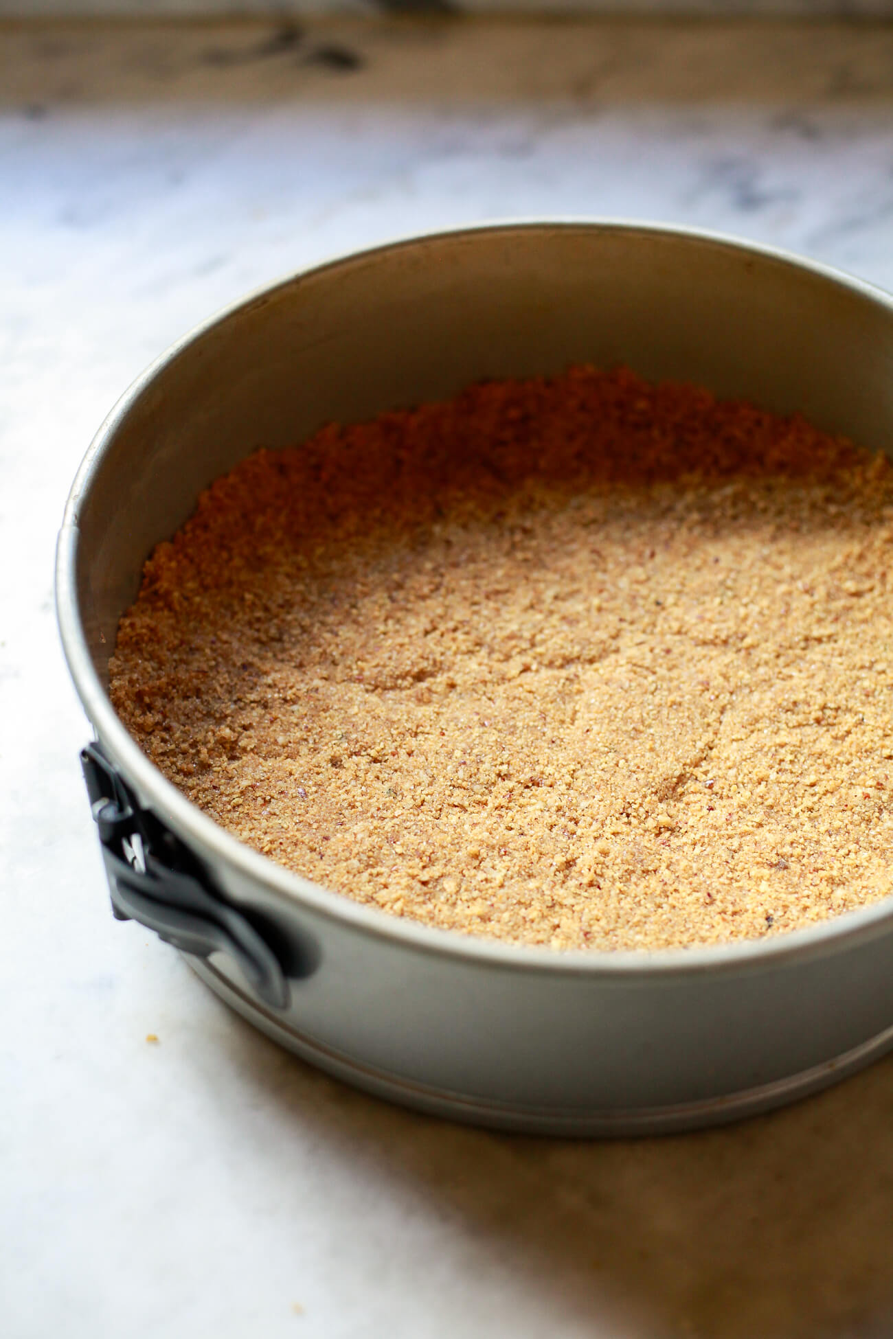 A graham cracker and pecan crust in the a springform pan to make a pumpkin cheesecake.
