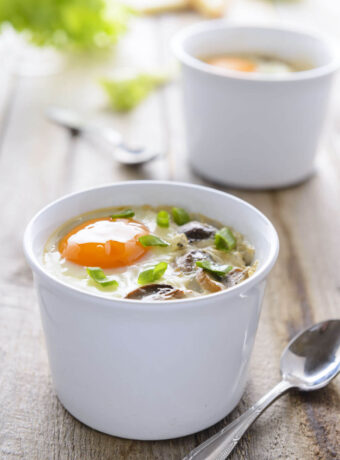 Two ramekins filled with Eggs en Cocotte. French baked eggs with cream.