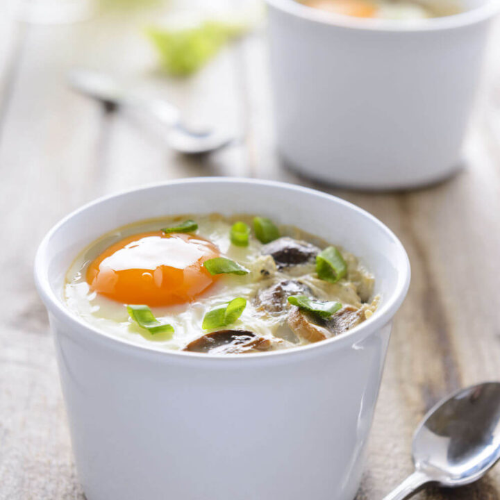 Two ramekins filled with Eggs en Cocotte. French baked eggs with cream.