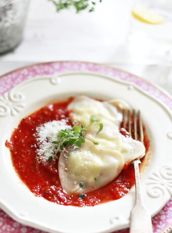 Heart-shaped cheese ravoili with wonton wrappers on a plate with tomato sauce.