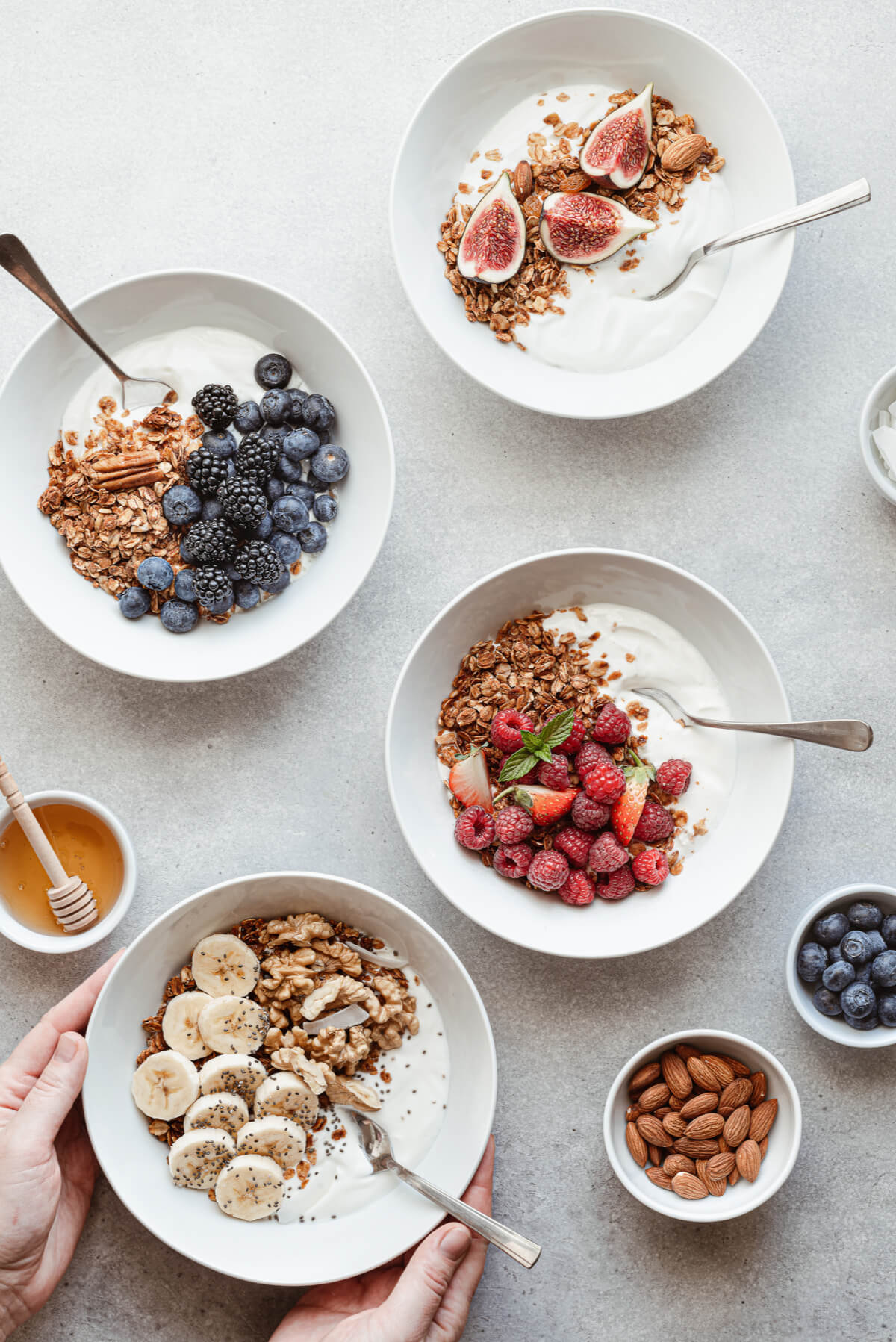 Four bowls filled with yogurt, granola, and berries, bananas, and figs. A healthy breakfast idea. 