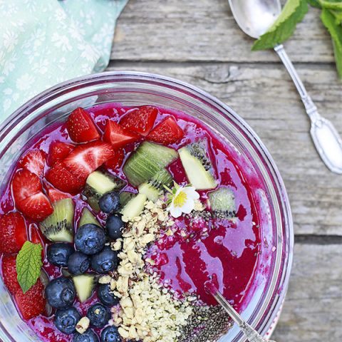 A bright pink dragon fruit or pitaya smoothie bowl topped with seeds and fresh fruit.