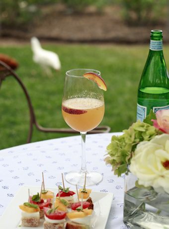 A peach bellini cocktail on an outdoor table next to caprese bruschetta appetizers.