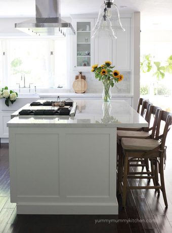 A clean white kitchen with a marble island and wooden barstools.