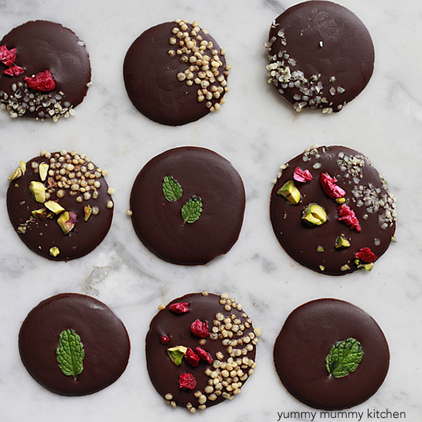 Round drops of dark chocolate topped with colorful healthy toppings like fresh mint and goji berries.