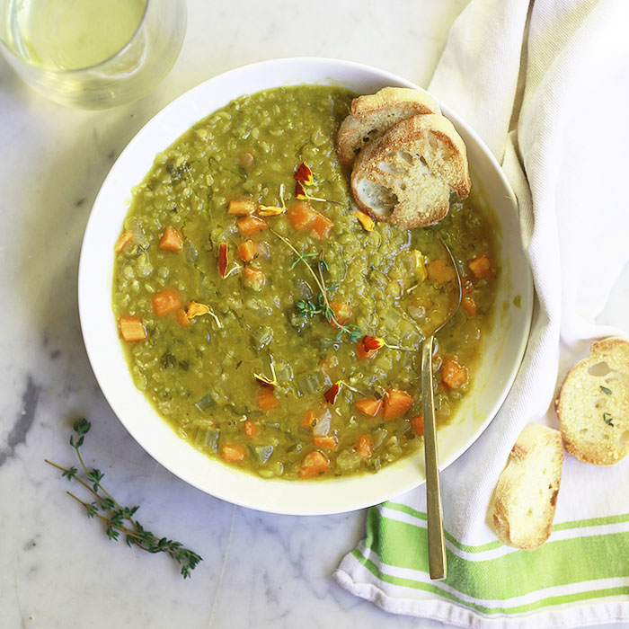 A bowl of vegetarian split pea soup with baguette on the side.
