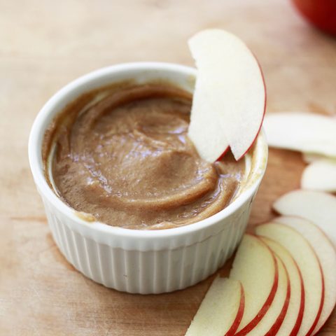 A small bowl filled with smooth date vegan caramel and an apple slice.