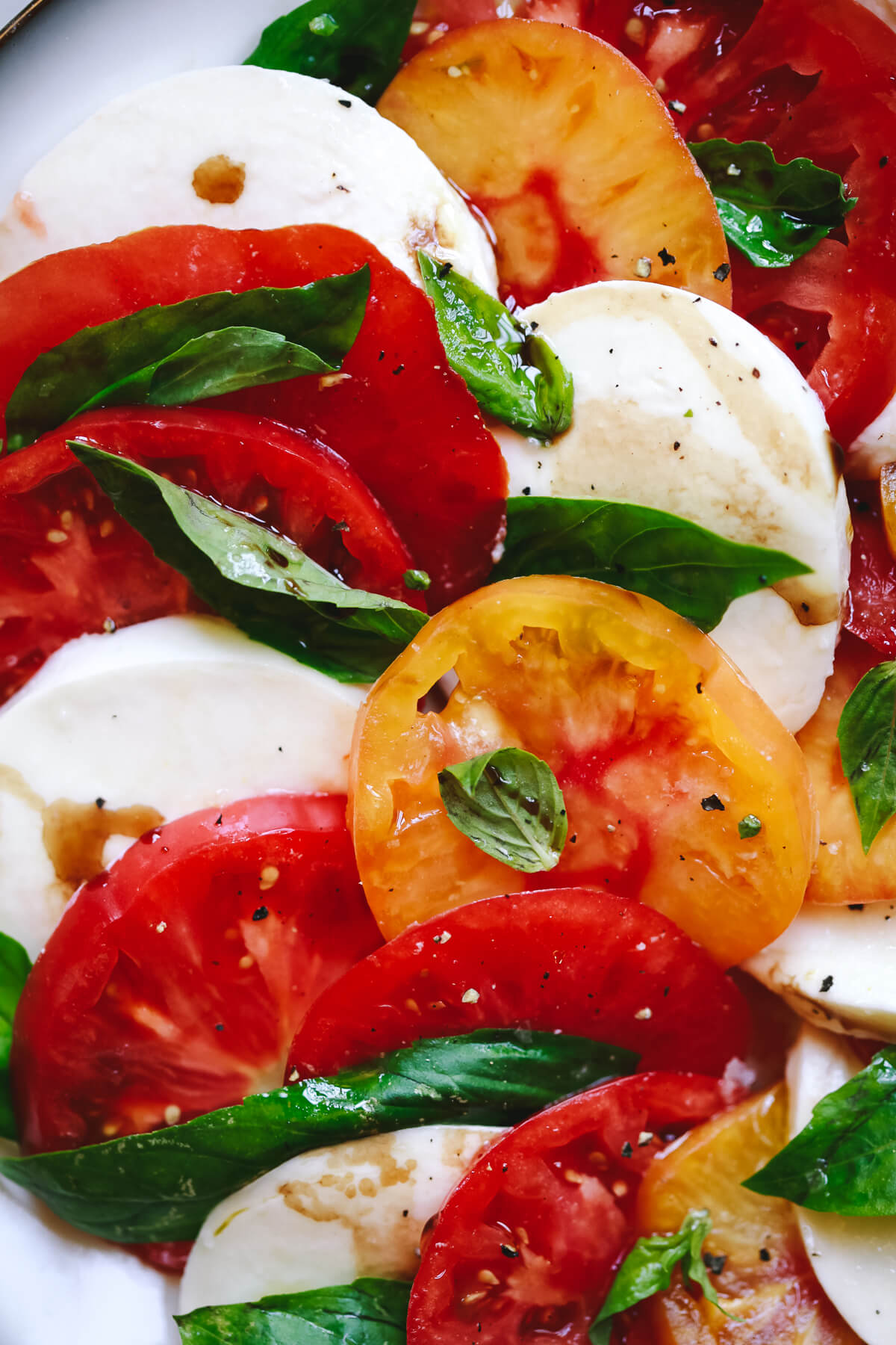 Red and yellow heirloom tomatoes, mozzarella slices, and basil leaves close-up photo depicting a delicious Caprese salad. 