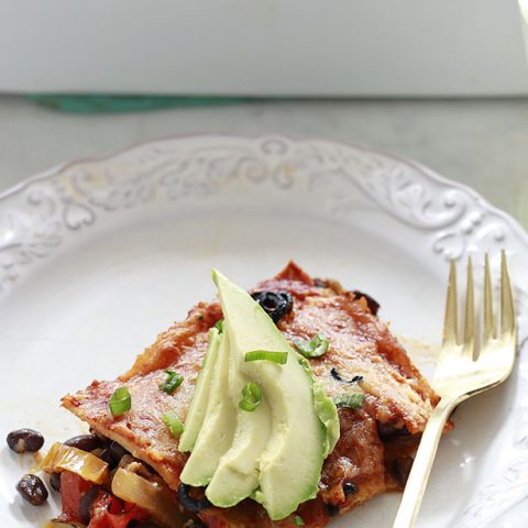 A piece of vegetarian enchilada casserole with avocado on a white plate.