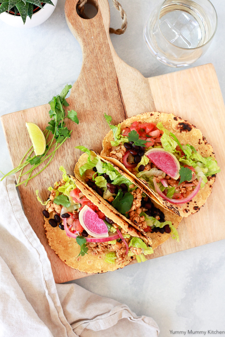 Three colorful vegan tacos with tempeh, black beans, lettuce, and watermelon radish. 