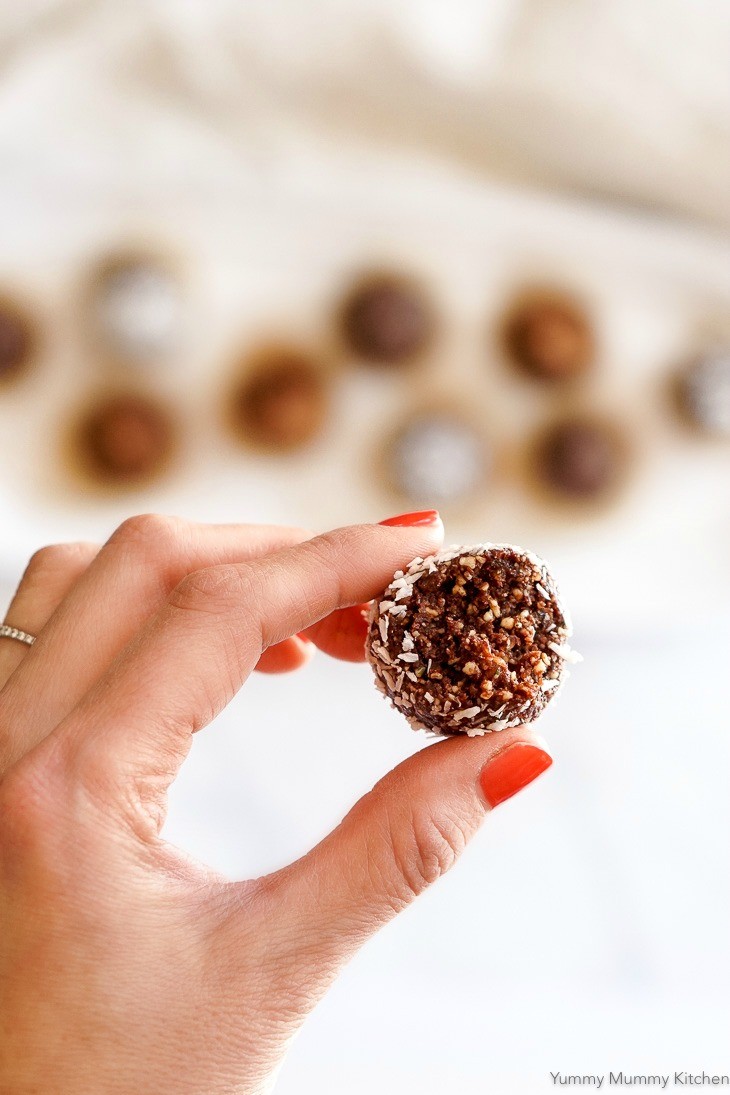 A hand holds one chocolate bliss ball made with dates, cacao and nuts. 