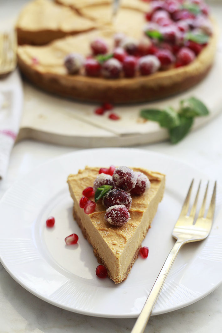 A slice of vegan pumpkin cheesecake topped with pomegranate and sugared cranberries. 