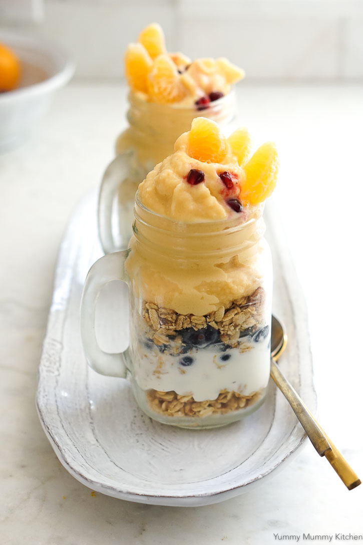 Layers of orange smoothie, granola, berries, and yogurt come together to make a delicious kid friendly parfait. 