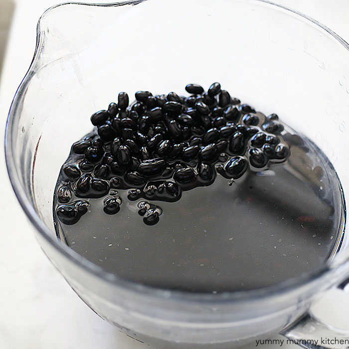 Dried black beans soaking in a bowl of water before cooking in a slow cooker. 