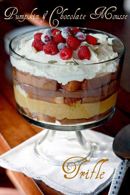 A trifle layered with pound cake, chocolate mouse and pumpkin filling in a trifle dish. Topped with whipped cream, raspberries, and candied cranberries. Text overlay reads, "pumpkin & chocolate mouse trifle." 