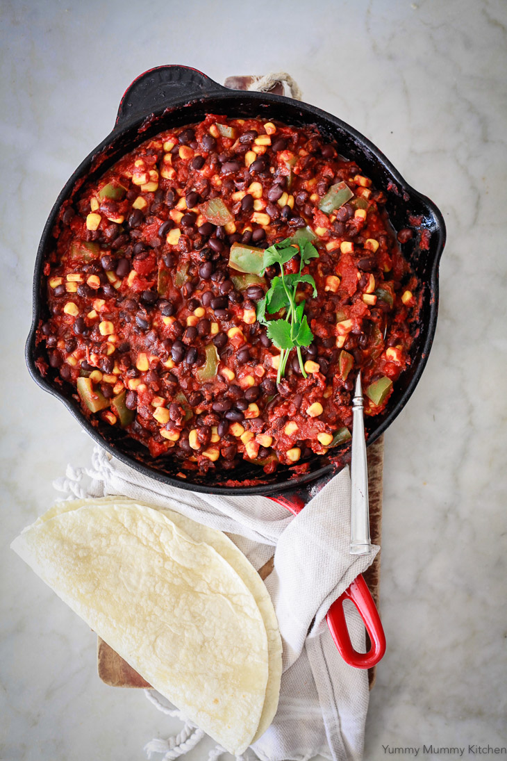 A skillet filled with black bean and corn enchilada filling to make vegetarian enchiladas. 