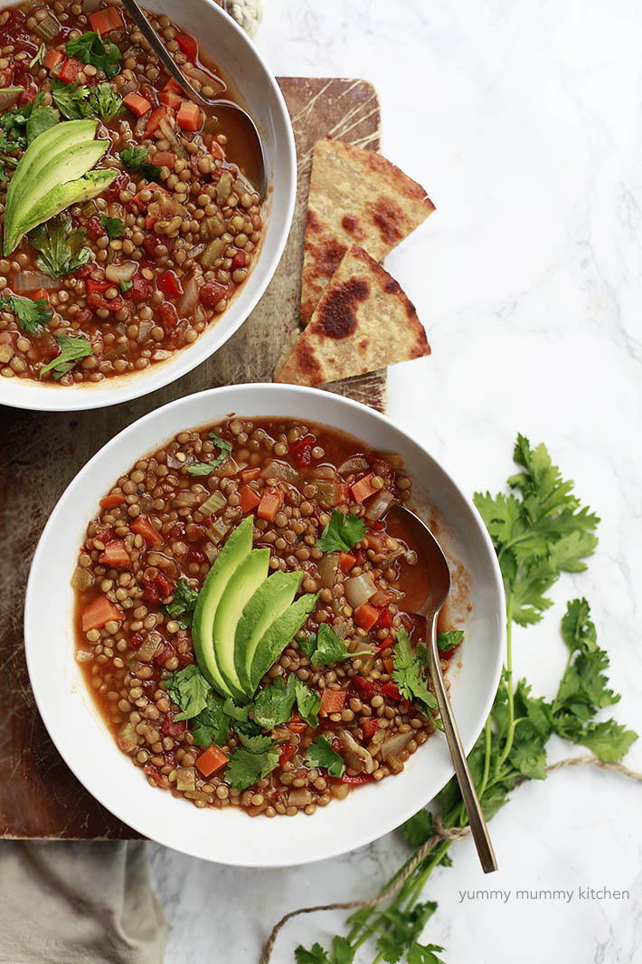 Healthy vegetarian and vegan Mexican lentil soup recipe in two bowls topped with avocado and cilantro. 