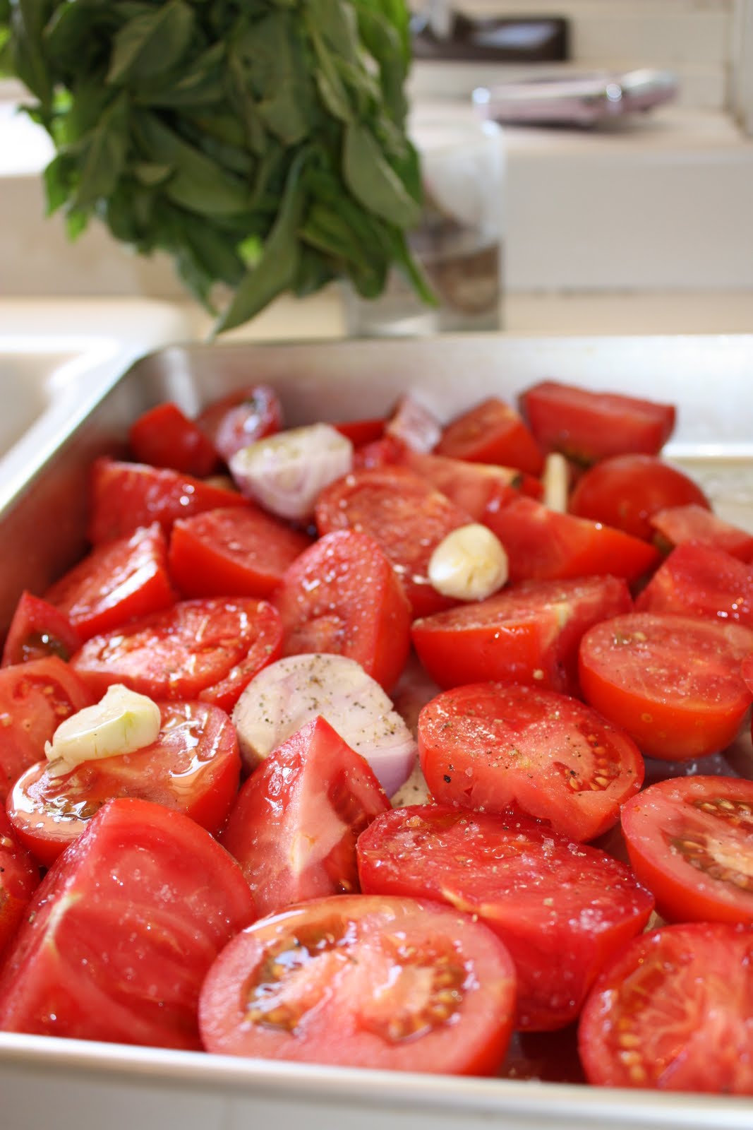 Cut tomatoes seasoned with salt, pepper, and olive oil on a sheet pan with garlic and shallots. 