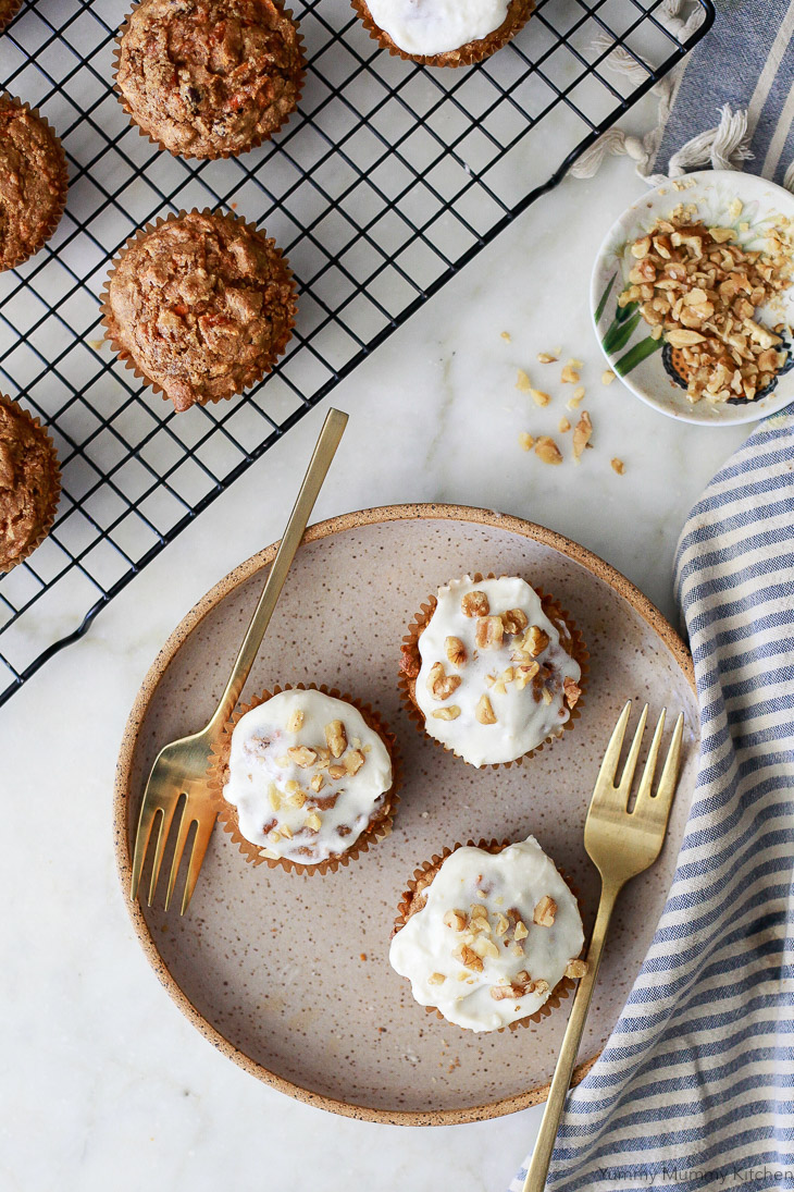 Carrot muffins on a plate with forks. These carrot muffins are frosted with dairy-free cream cheese frosting and topped with walnuts. They are vegan and gluten free. 