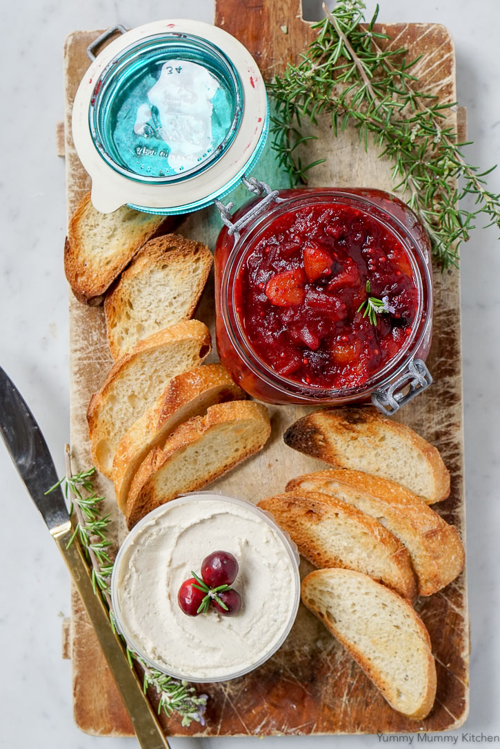 Red spiced cranberry chutney on a cutting board with soft vegan cheese and bread. 