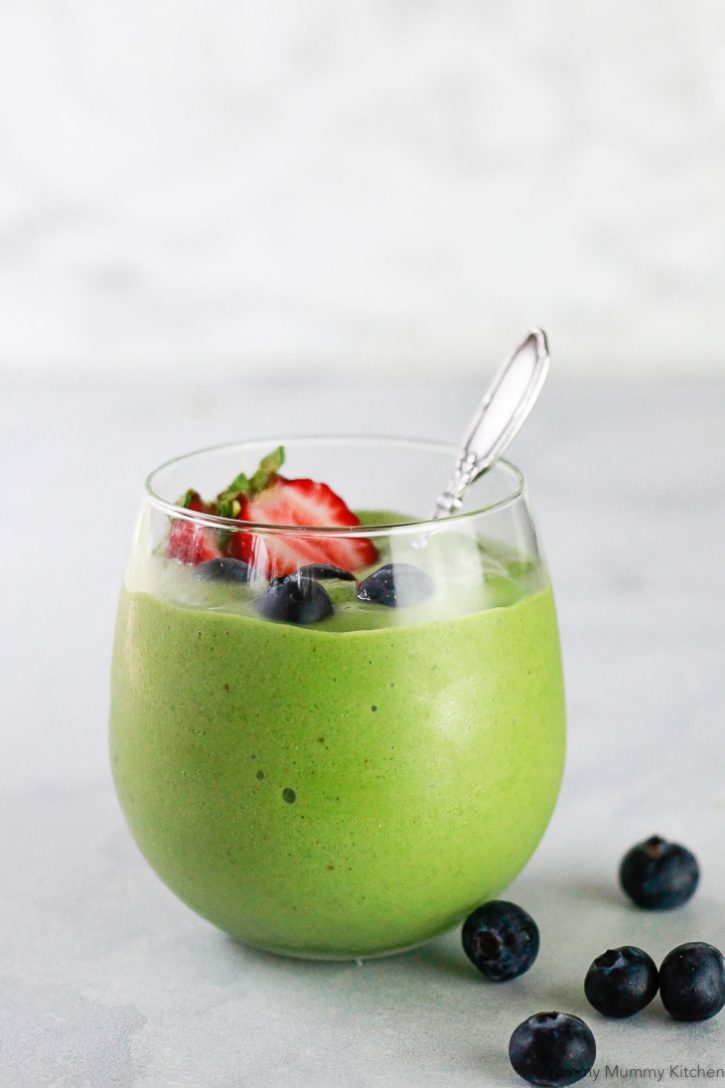 Green matcha powder smoothie in a clear glass with a spoon and berries. This healthy matcha smoothie is a delicious vegan and gluten free breakfast or snack. 