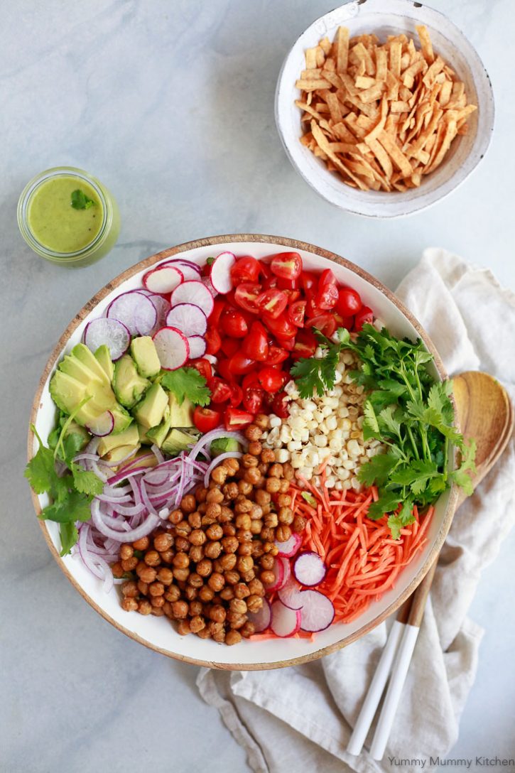 A beautiful Southwestern style salad with sections of roasted chickpeas, radish, corn, tomatoes, red onion, and cilantro. A jar of avocado dressing and bowl of tortilla crisps on the side. This Southwest salad is naturally vegetarian, vegan, and gluten-free. 