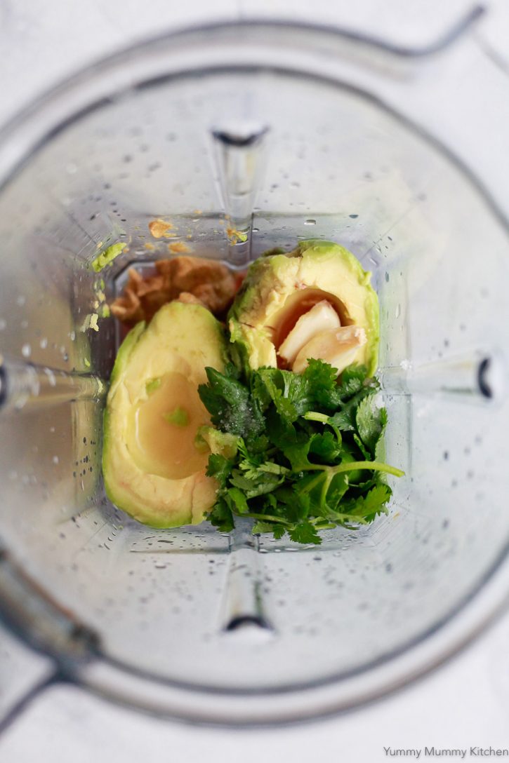 Avocado, cilantro, mustard, lime juice in a blender ready to blend some vegan avocado salad dressing. 