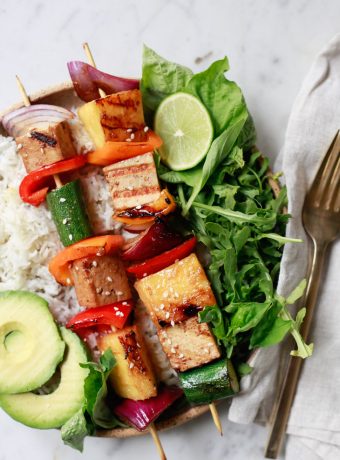 Beautiful grilled vegetable, pineapple, and tofu kabobs on a plate with rice.