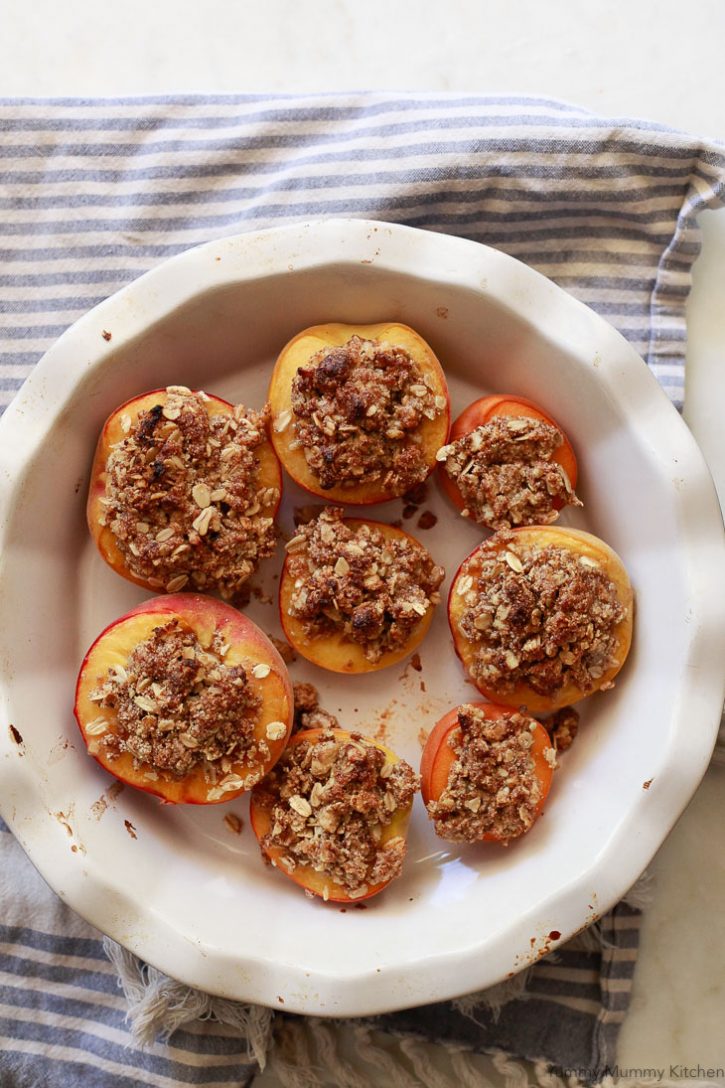 Baked peaches with oatmeal crisp topping in baking dish are a beautiful summer dessert that's vegan and gluten free. 