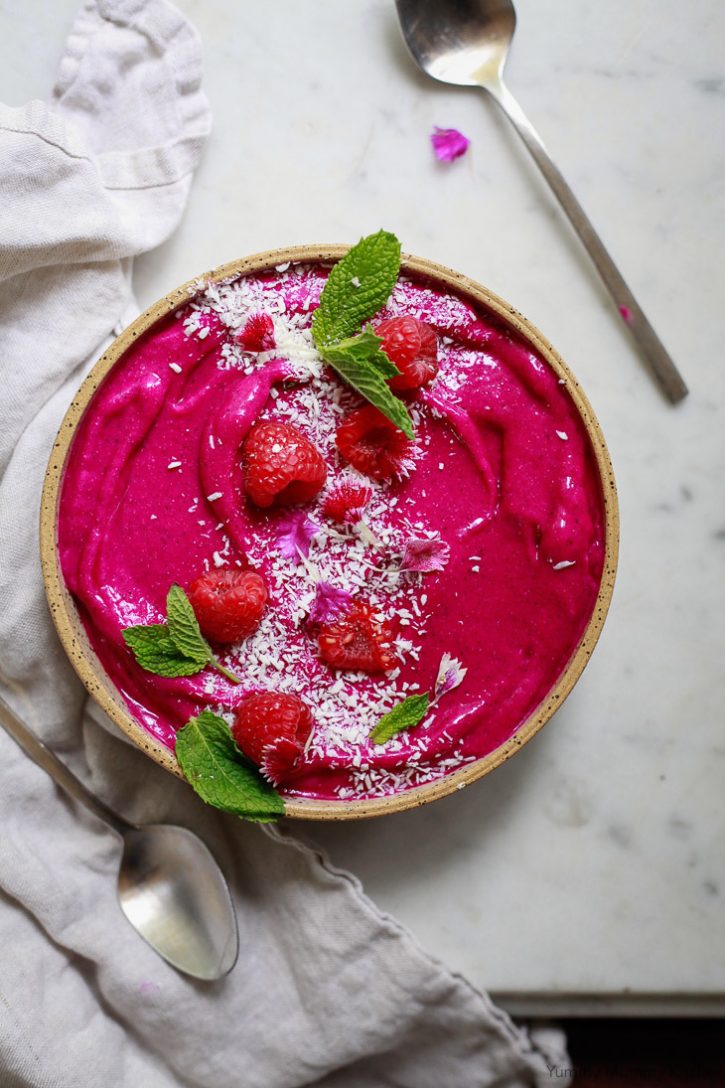 Bright pink dragon fruit smoothie bowl with raspberries, coconut, mint, and edible flowers. A beautiful dragon fruit smoothie bowl is easy to make! 