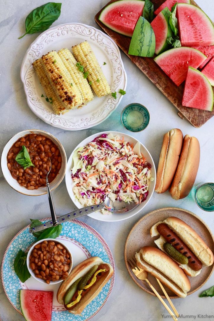 Beautiful photo of a vegetarian summer BBQ with veggie dogs, vegetarian baked beans, vegan coleslaw, watermelon and corn. 