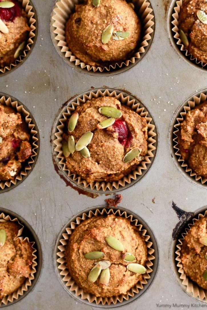 Pumpkin muffins in a tin with fresh cranberries and pepitas. These deliciously healthy pumpkin muffins are vegan and gluten free. 