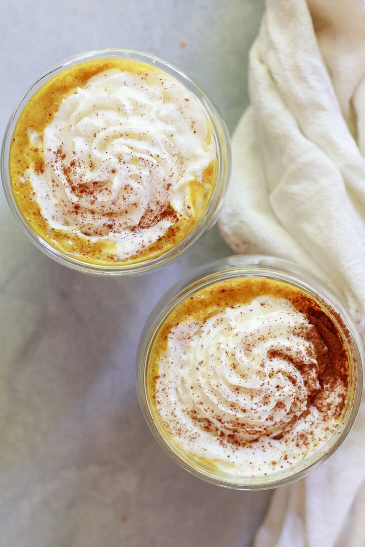 Two golden pumpkin spice lattes topped with whipped cream and pumpkin pie spice. This healthy pumpkin spice latte recipe is vegan and made with turmeric golden milk. 