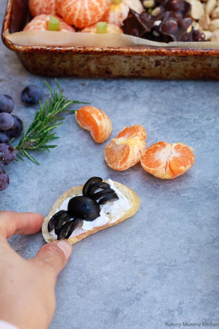 A cute Halloween spider made out of an olive on top of crostini and cheese. What a cute and delicious Halloween party appetizer finger food idea. 