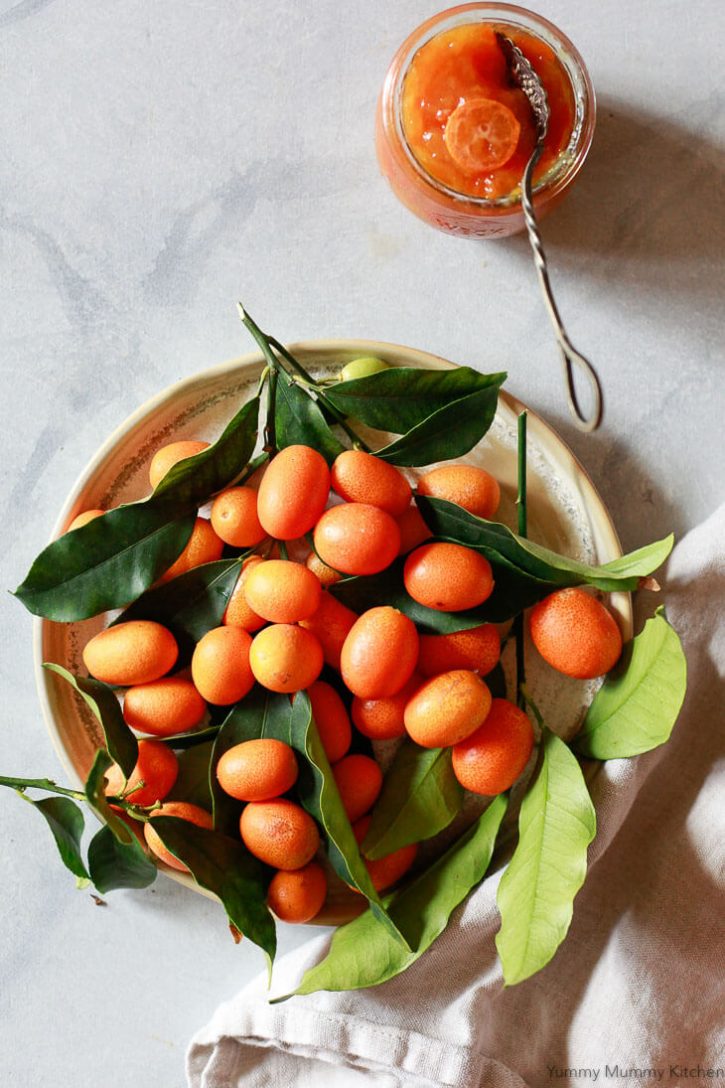 A beautiful photo of a dish filled with homegrown kumquats with leaves and a small jar of kumquat marmalade. 