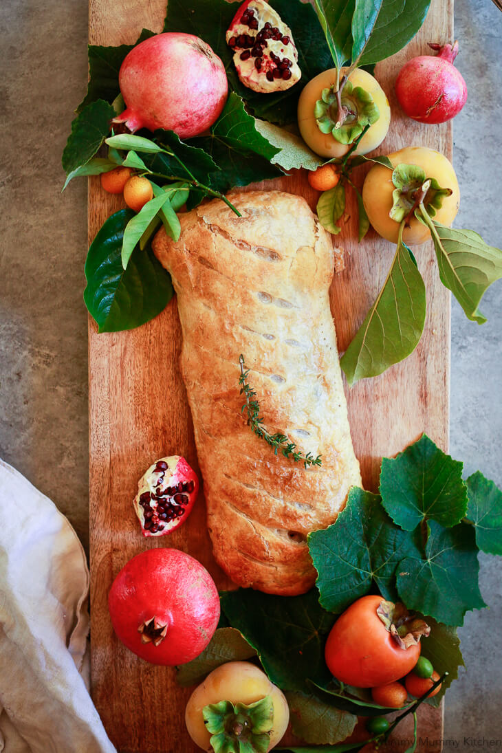 A beautiful puff pastry wrapped Wellington on a wooden cutting board decorated with fall ingredients. 