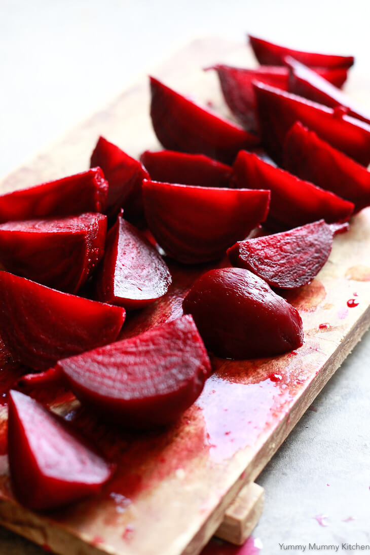 Freshly roasted beets peeled and quartered on a wooden cutting board. 
