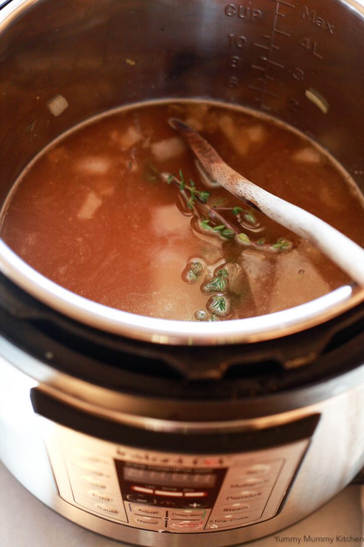 Broth and fresh thyme covers onions and arborio rice in an Instant Pot pressure cooker before cooking risotto. 