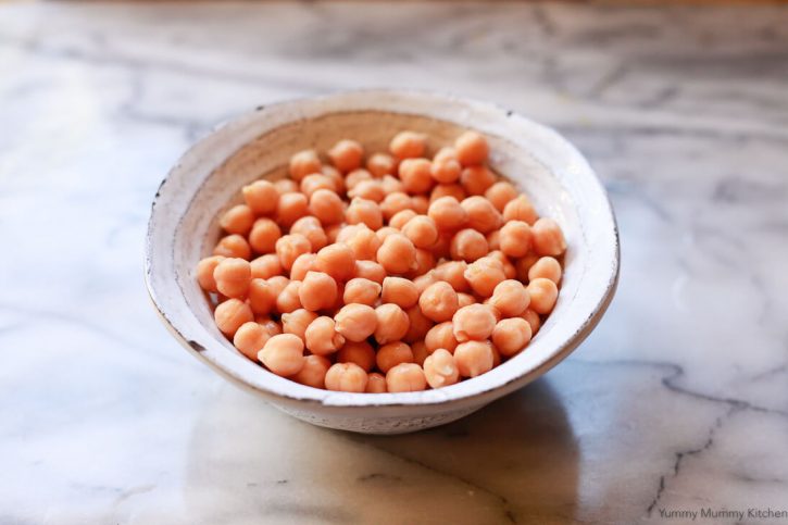 A bowl of chickpeas sit on a marble countertop. 