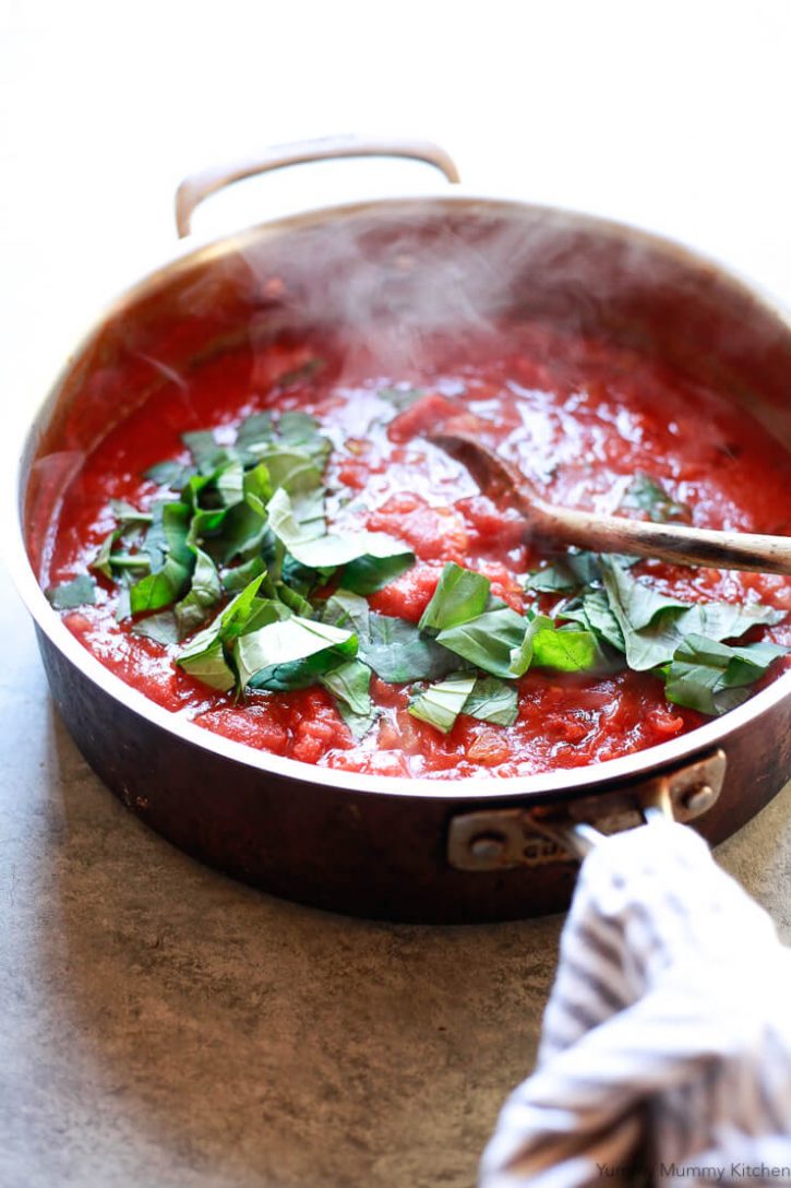 A large pan filled with bright red steaming pomodoro tomato sauce topped with fresh basil. 