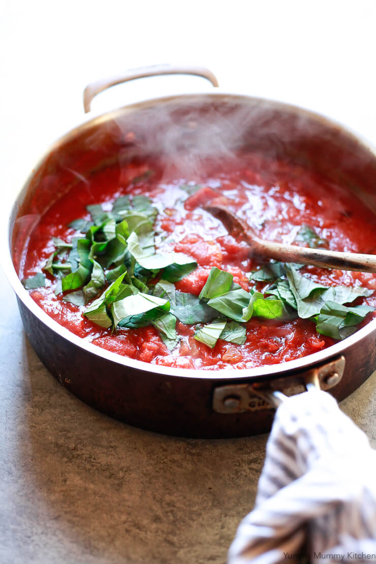 A sauce pan filled with steaming red sauce topped with fresh basil. 