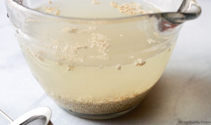 A cup of white quinoa is rinsed in a bowl of water before cooking. 