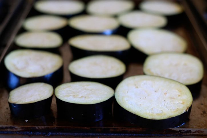 Sliced eggplant rounds begin to cook on a griddle to make healthy vegan eggplant parmesan. 