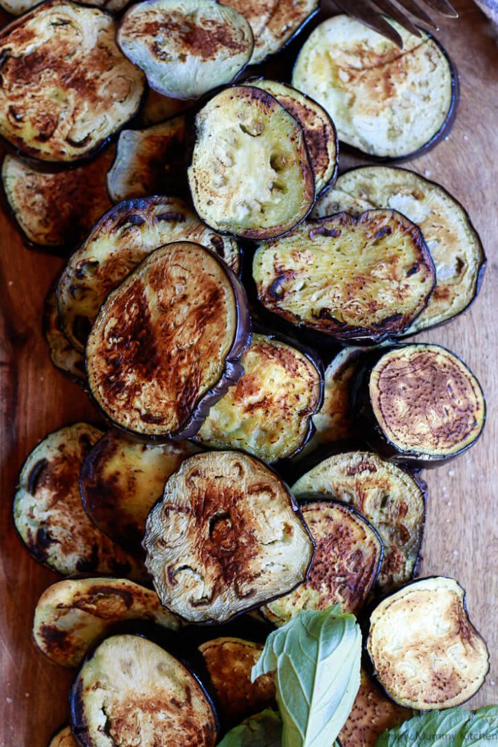 Beautiful browned eggplant slices sit on a cutting board ready to be assembled into a healthy vegan baked eggplant parmesan. 