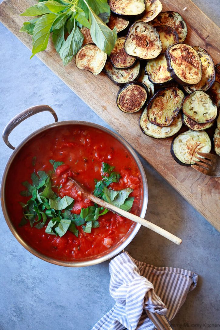 A pan filled with pomodoro sauce sits on a countertop alongside cooked eggplant slices ready to be assembled into healthy baked vegan eggplant parmesan. 