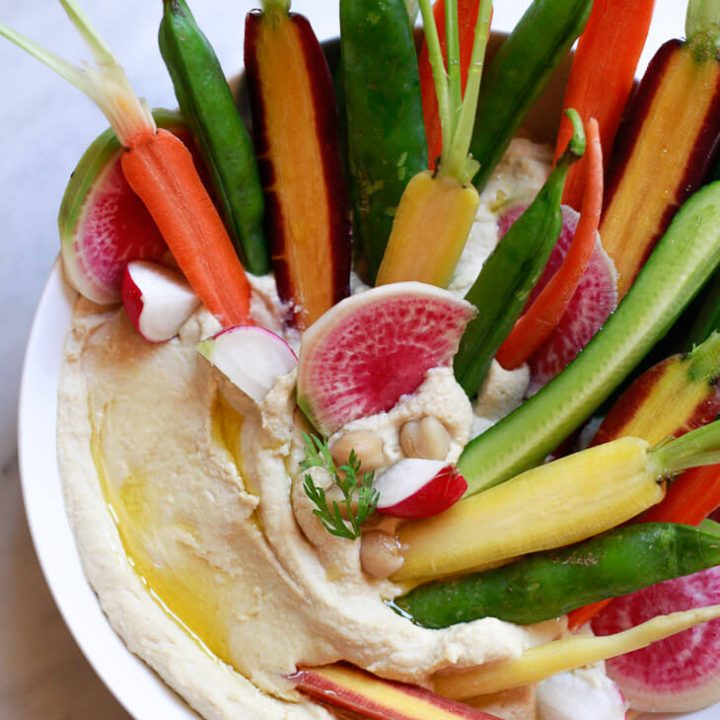 A beautiful bowl of classic homemade hummus topped with colorful carrots, watermelon radish, and cucumber.