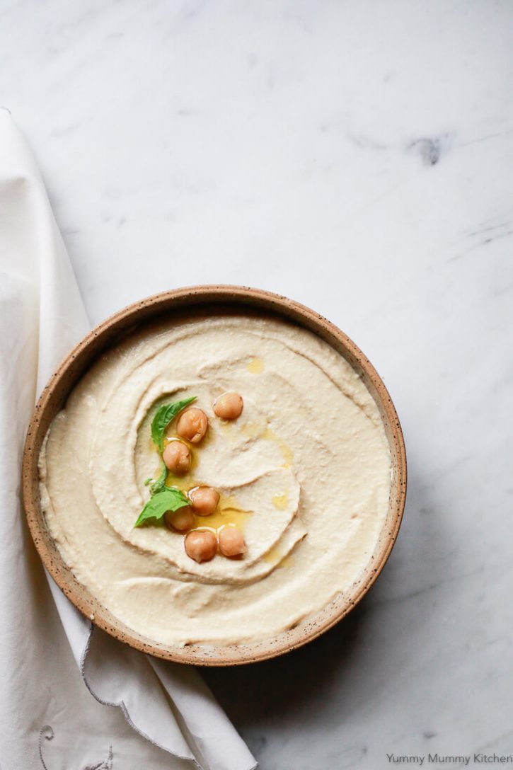 A earthenware bowl filled with homemade hummus sits on a marble countertop. 
