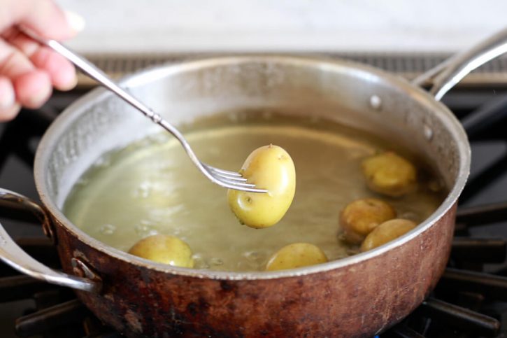 Small yellow potatoes boil in a large copper pot. 